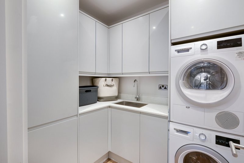 Modern utility room with white cabinetry, stacked washing machine and tumble dryer, sink.