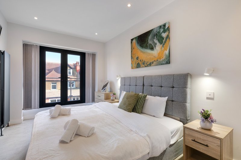 Modern bedroom with double bed, gray headboard, wooden nightstand, and black patio doors