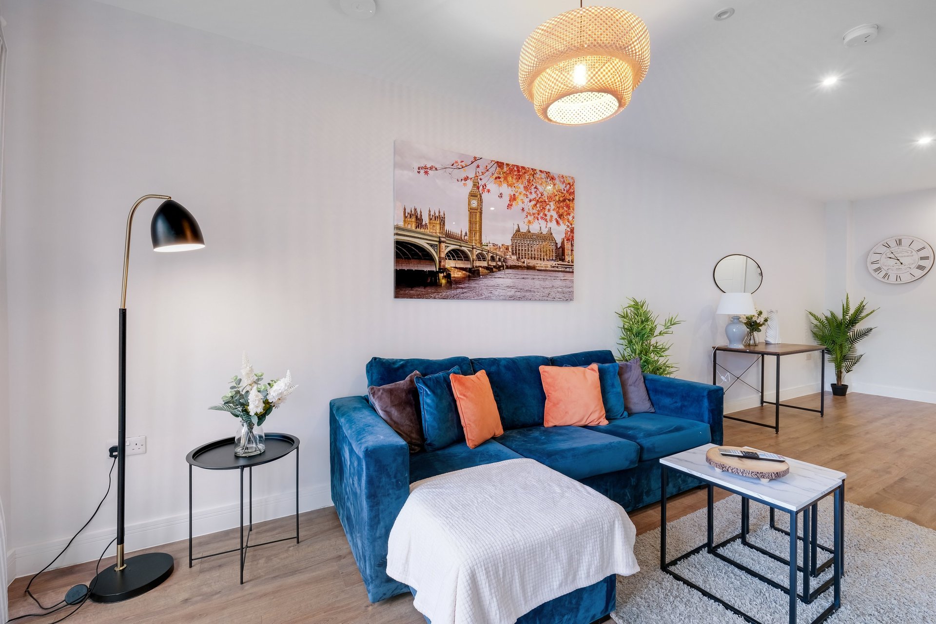 Modern living room with blue velvet sofa, orange cushions, floor lamp, and framed city artwork