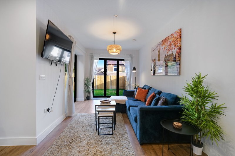 Modern living room with blue sofa, wall-mounted TV, pendant light, and glass doors to outdoor area