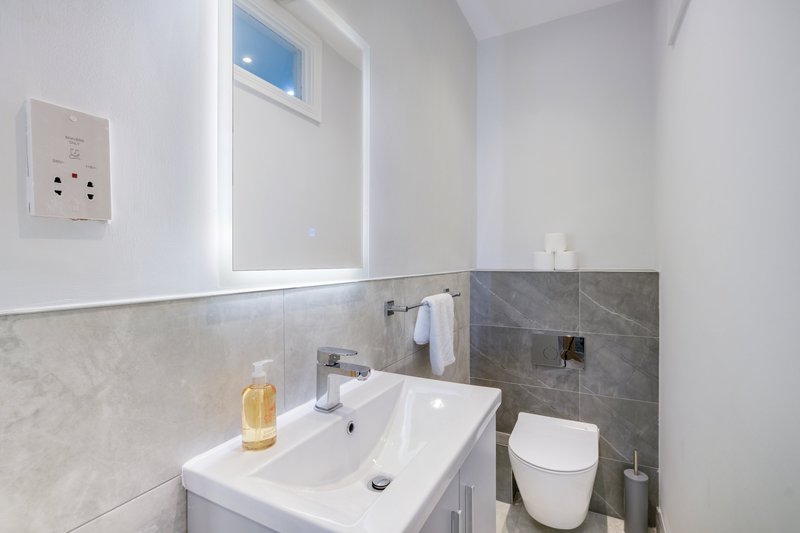 Modern bathroom with white sink, toilet, mirror, and grey tile accents