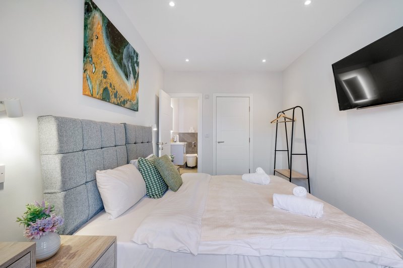Bright modern bedroom with grey upholstered headboard, white bedding, wall art and mounted TV