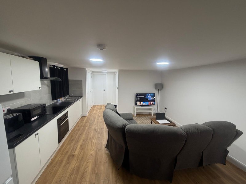 Open-plan kitchen and lounge with dark sofa, white cabinetry, wooden flooring and TV