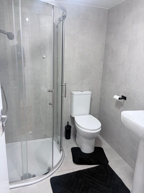 Modern bathroom with shower enclosure, white toilet, sink and black mat