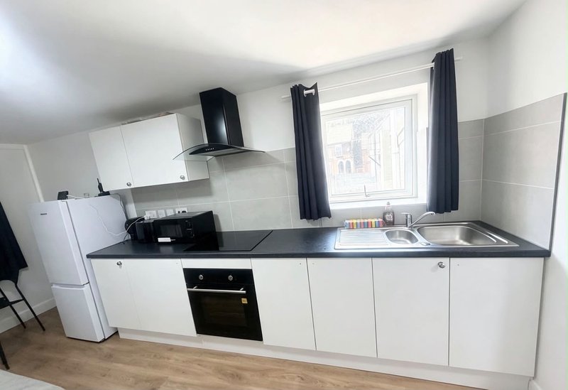Modern kitchen with white cabinetry, black countertop, integrated oven and sink