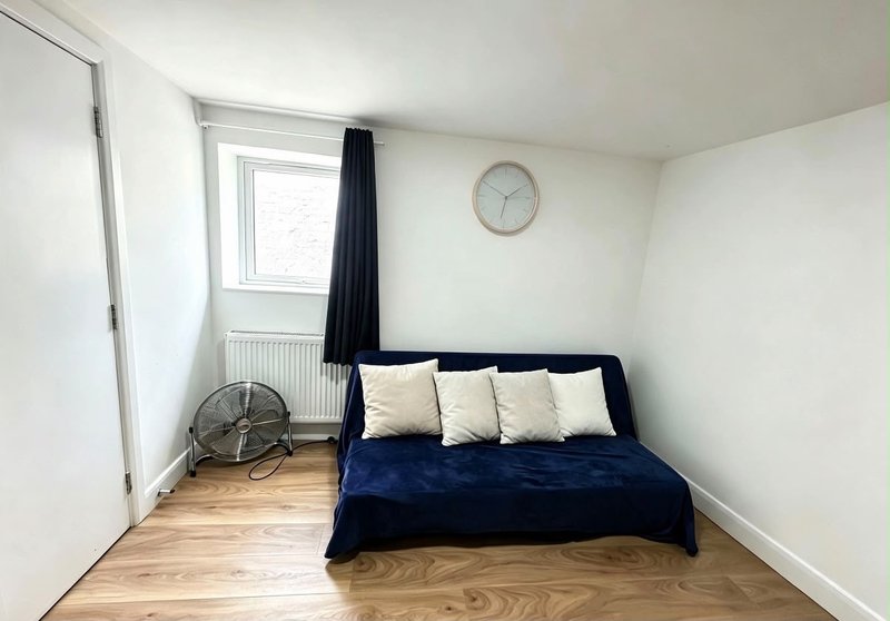 Bedroom with double bed, blue duvet, cream pillows, wooden floor and wall clock