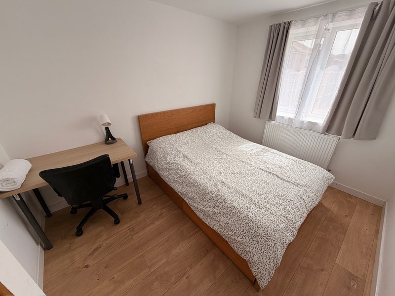 Bedroom with single bed, wooden headboard, desk, chair and window with curtains