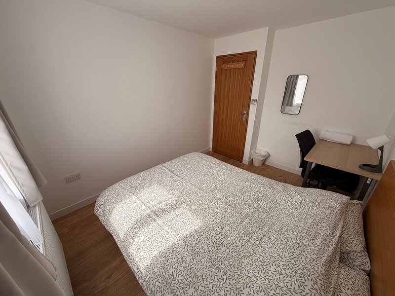 Bedroom with double bed, wooden door, desk, wooden floor and window