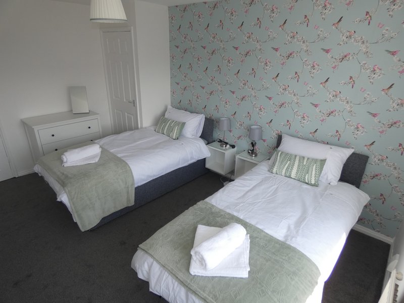 Twin bedroom with two single beds, floral wallpaper, white bedding and green throws