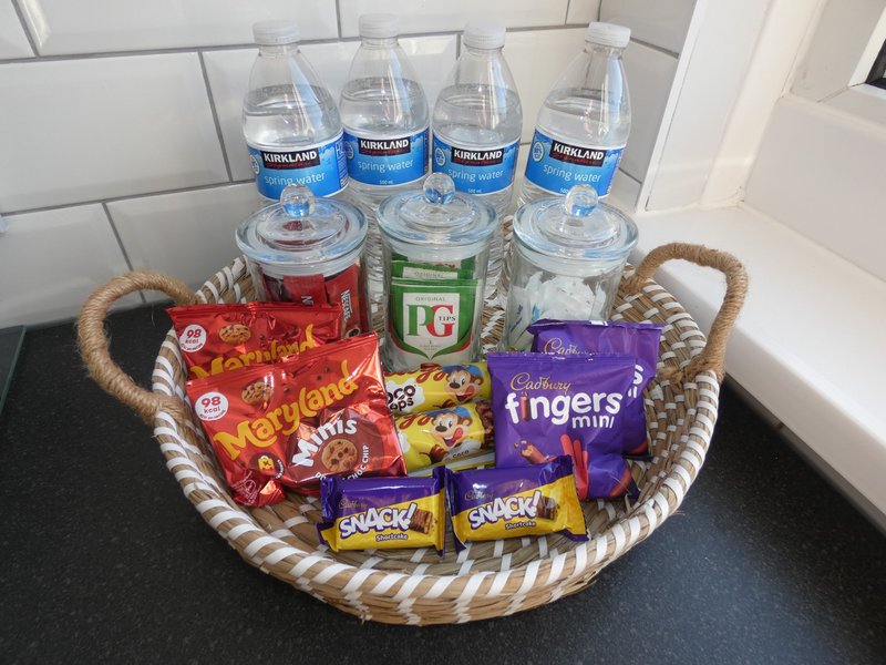 Kitchen counter with welcome basket containing bottled water, tea, snacks and packaged treats