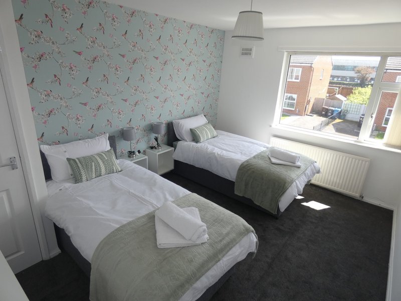 Twin bedroom with floral wallpaper, white bedding, green throws, window with city view