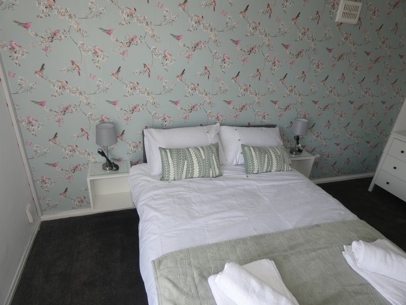 Bedroom with double bed, floral wallpaper, white bedding, striped pillows and bedside tables