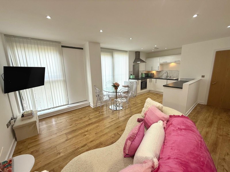 Open-plan living room and kitchen with wooden flooring, pink sofa, TV, and modern fitted kitchen