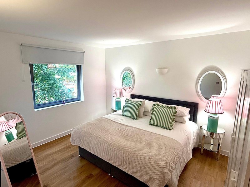 Bright modern bedroom with double bed, green cushions, wooden floor and round mirrors