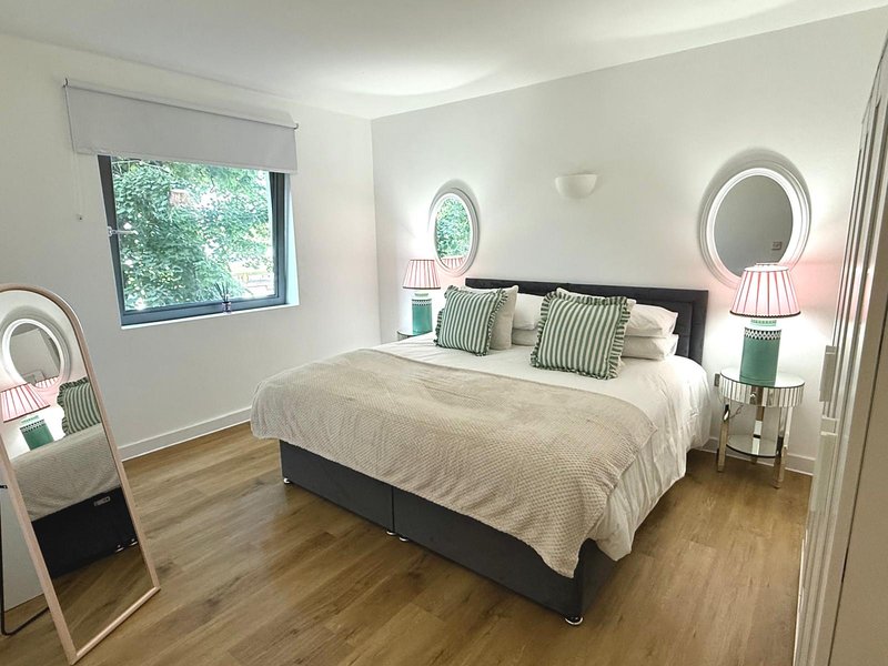 Modern bedroom with double bed, round mirrors, pink lamps and wooden flooring