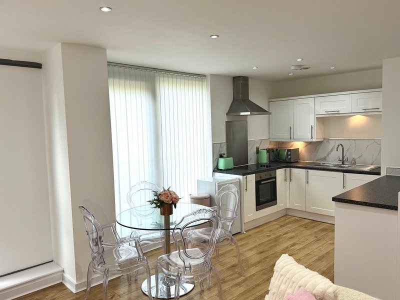 Modern open-plan kitchen and dining area with white cabinetry, glass table, and wooden flooring