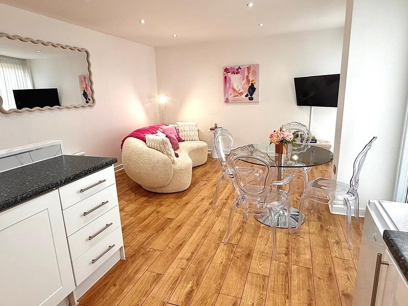 Open-plan studio with cream bean bag chair, kitchenette, wooden flooring and wall-mounted TV