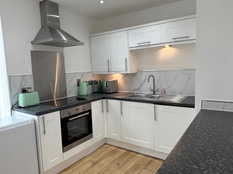 Modern kitchen with white cabinetry, black countertops, stainless steel appliances and marble backsplash