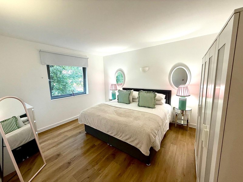 Bright bedroom with double bed, wooden floor, round mirrors and green accent pillows