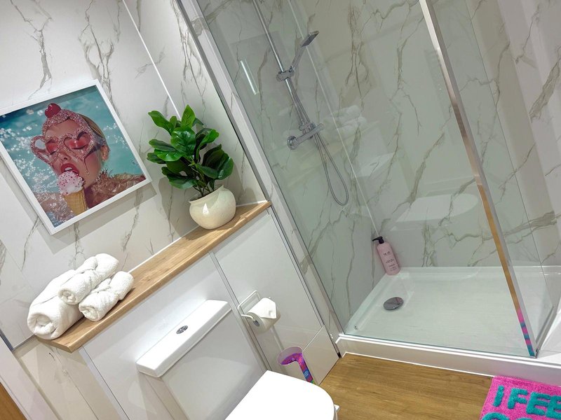 Modern bathroom with marble tiles, walk-in shower, toilet, and wooden shelf with toiletries and plant
