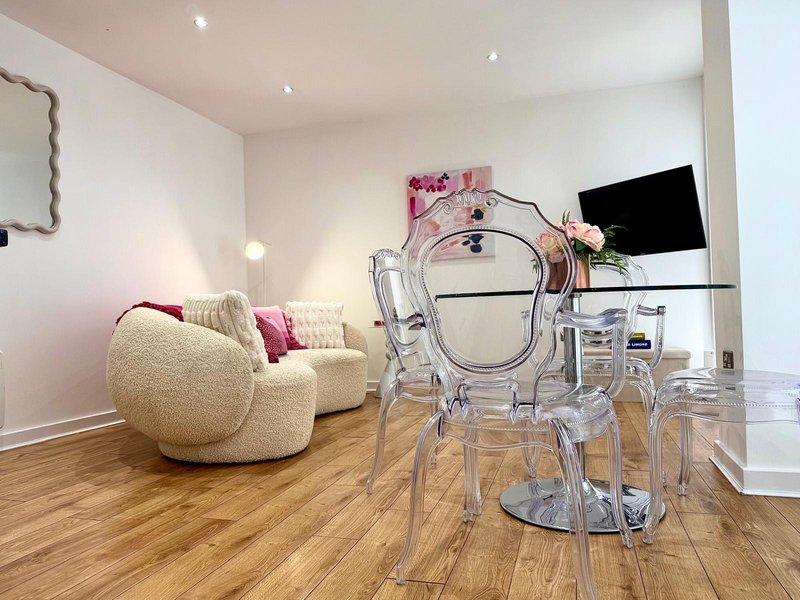 Modern living room with cream armchair, transparent acrylic chair, wooden floor and pink artwork