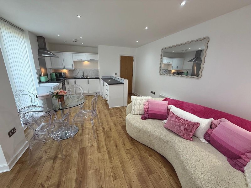 Open-plan kitchen and living area with cream sofa, pink cushions, wooden flooring and modern appliances
