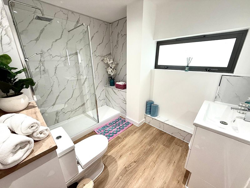 Modern bathroom with marble shower enclosure, white toilet, sink and wooden floor