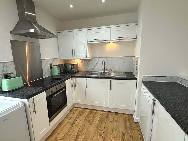 Modern kitchen with white cabinets, black granite countertops, stainless steel appliances and wooden flooring