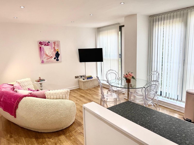 Modern bedroom with pink accents, curved upholstered chair, mounted TV, wooden flooring and vertical blinds