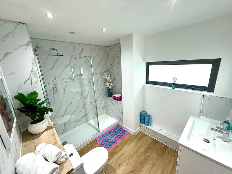 Modern bathroom with walk-in shower, marble tiles, wooden flooring, white sink and toilet