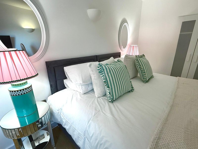 Bright modern bedroom with double bed, striped green cushions, pink lampshade and round mirror
