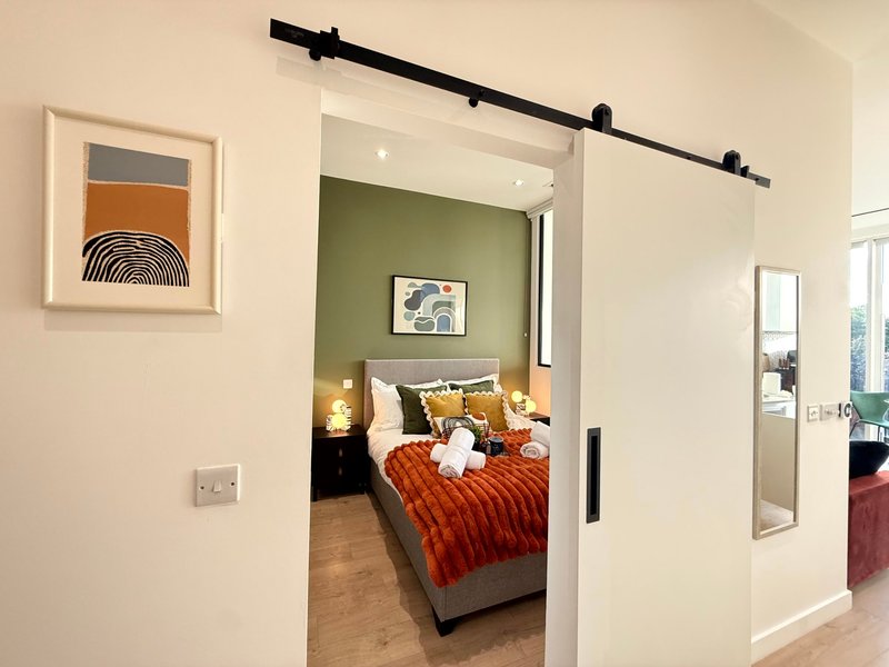 Modern bedroom with double bed, orange bedding, green accent wall and sliding barn door