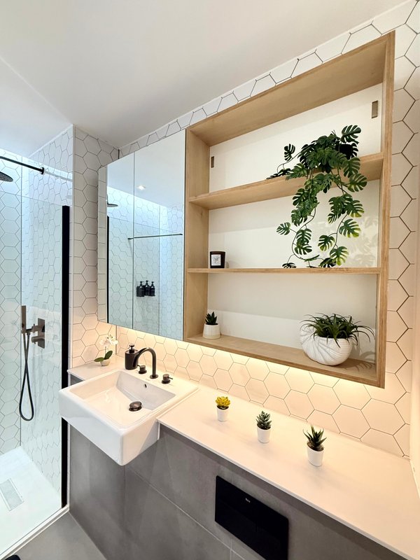 Modern bathroom with white hexagonal tiles, floating sink, mirror, wooden shelving with plants and decorative items
