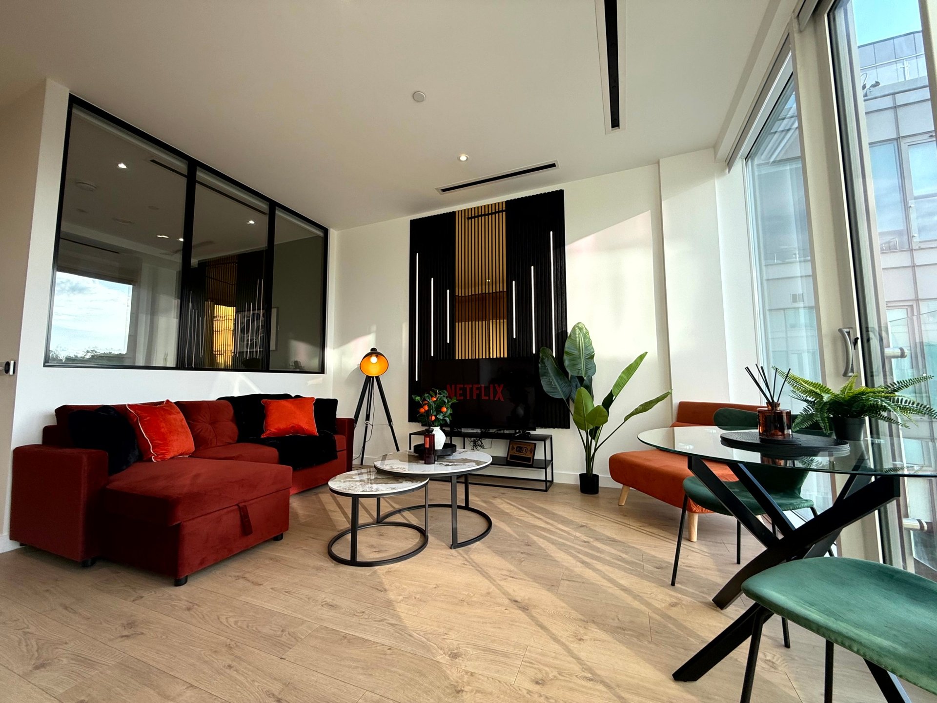 Modern living room with red sectional sofa, black accent wall, potted plants, and floor-to-ceiling windows