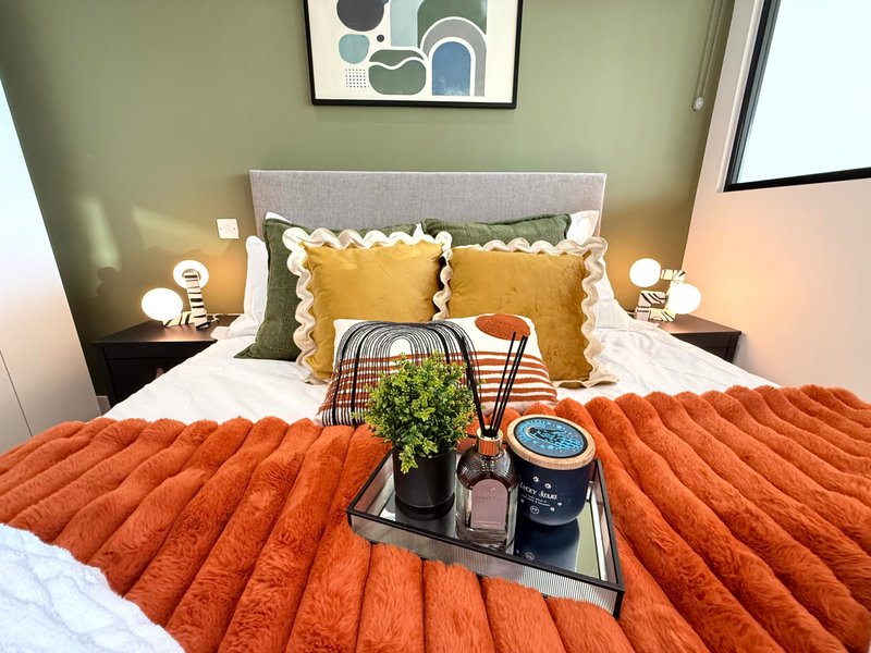 Modern bedroom with orange quilted bedding, yellow pillows, green accent wall and abstract art