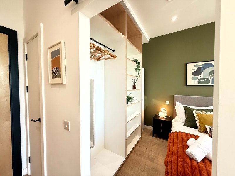 Modern bedroom with green accent wall, bed with orange throw, wooden flooring and built-in wardrobes