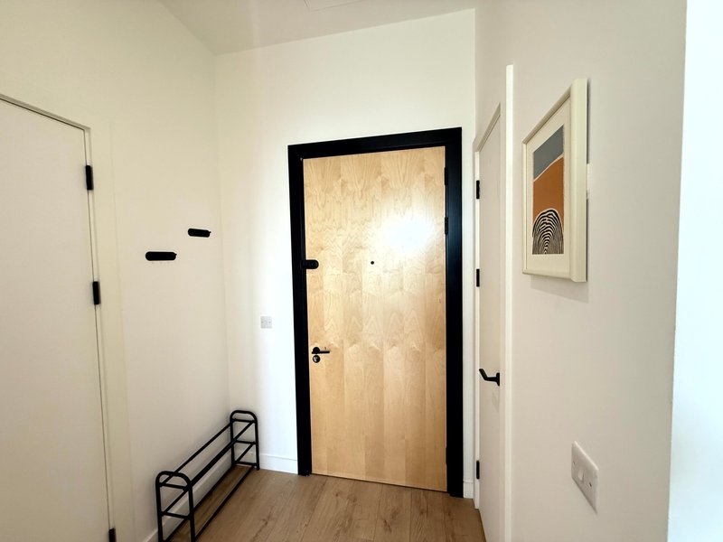 Bright hallway with wooden door, shoe rack, and framed wall art