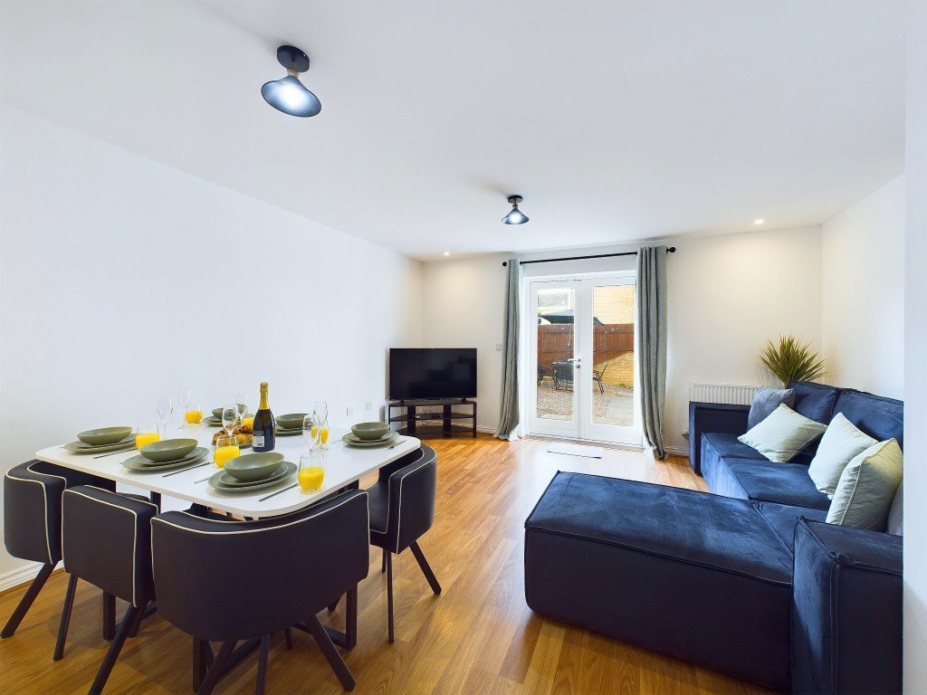 Open-plan living area with dining table, blue sofa, TV, and glass doors to garden