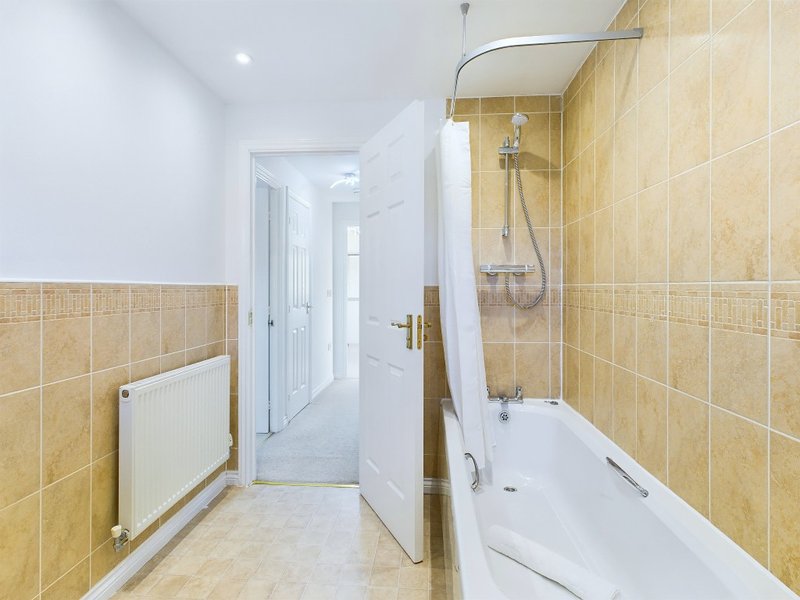 Bathroom with beige tiled walls, bathtub with shower, radiator and white door