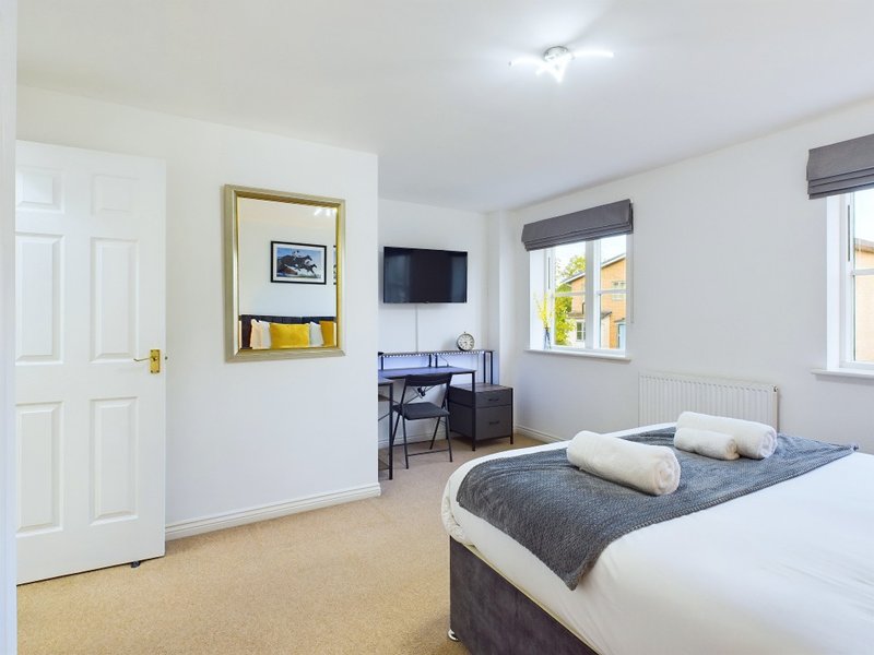 Bright bedroom with double bed, work desk, wall-mounted TV, and framed artwork