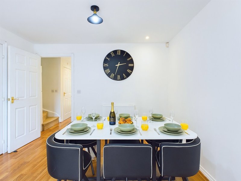 Dining room with set table, black chairs, wall clock, and wooden flooring