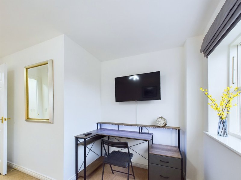 Modern bedroom with wall-mounted TV, desk workspace, chair, and yellow flowers in vase