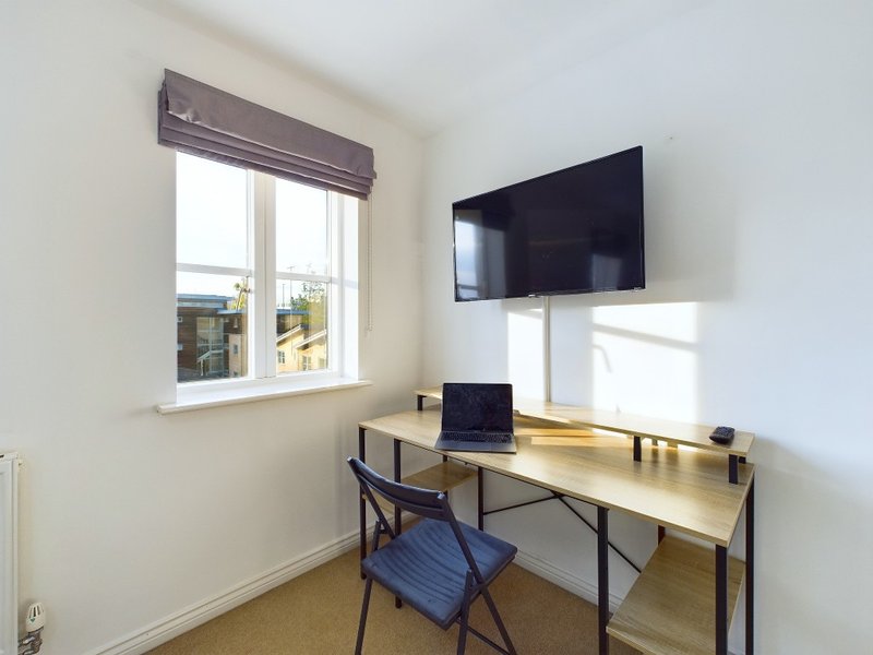 Modern home office with desk, laptop, wall-mounted TV, window and wooden flooring