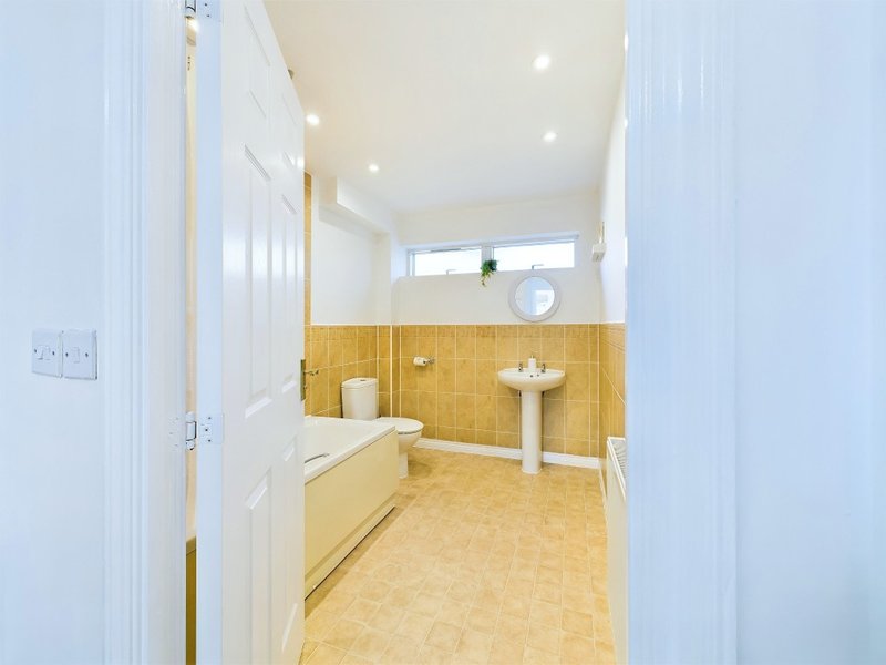 Bright bathroom with pedestal sink, toilet, yellow tile walls and cream flooring