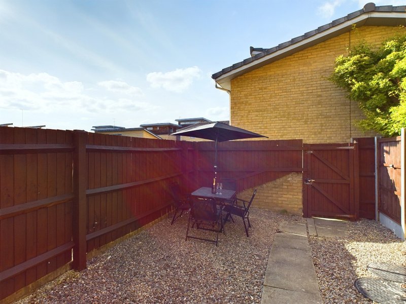 Enclosed garden patio with wooden fencing, gravel ground, outdoor seating and purple parasol