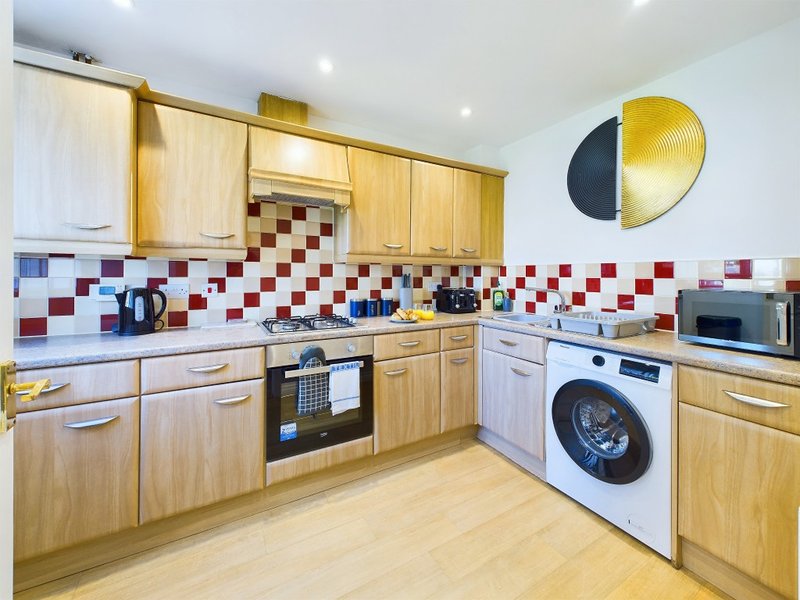 Modern kitchen with wooden cabinets, red and white tile backsplash, integrated appliances and decorative wall art