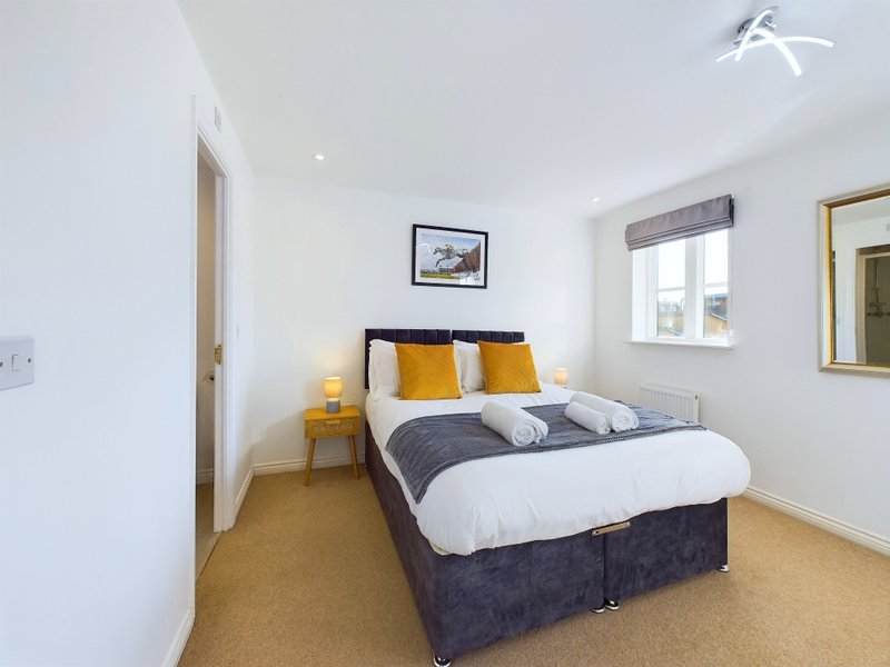 Modern bedroom with double bed, yellow and grey cushions, white bedding, and cork flooring