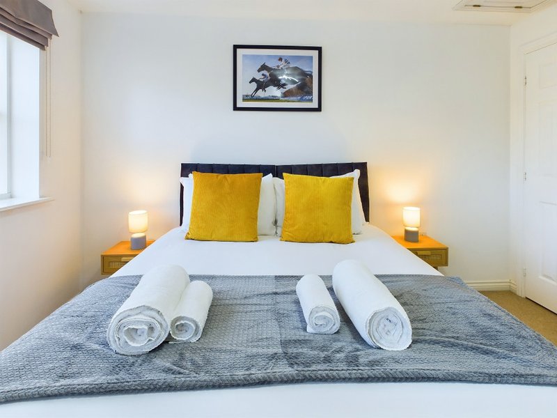 Bedroom with double bed, yellow cushions, rolled towels, and framed mountain artwork