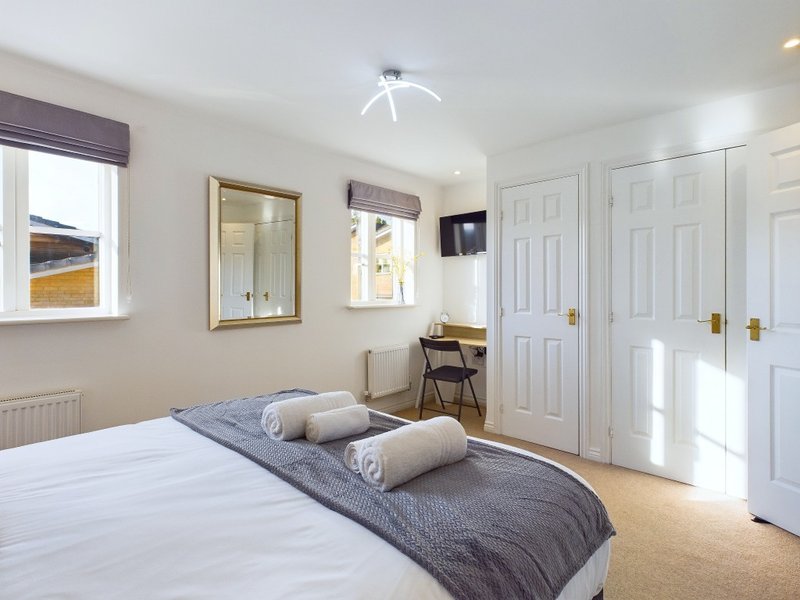 Bright bedroom with double bed, grey bedding, desk, mirror, and white fitted wardrobes