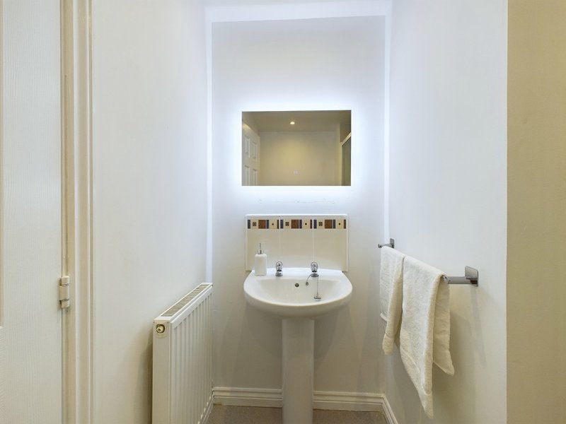 Modern bathroom with pedestal sink, illuminated mirror, radiator and towel rack